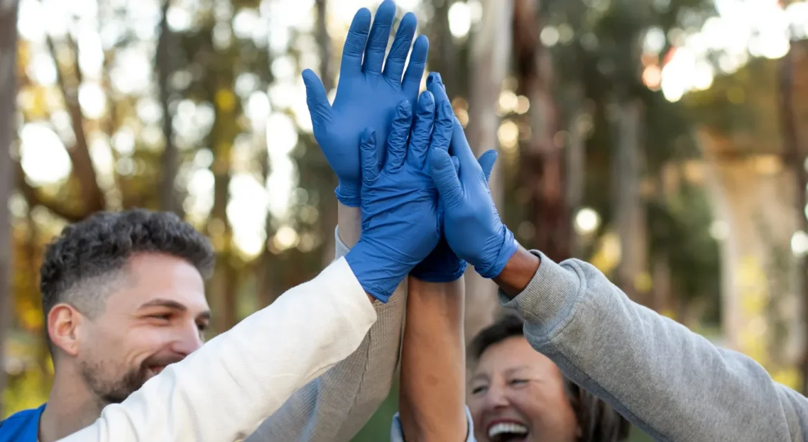 Grupo de personas con guantes azules celebrando, levantando las manos en un ambiente natural, mostrando alegría y trabajo en equipo.